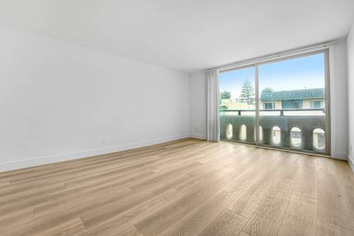 A room with wooden flooring and a large window overlooking a building.