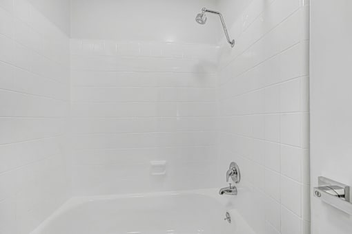 A white tiled shower with a shower head and faucet.