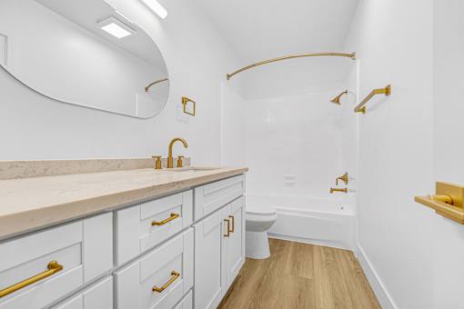 A white bathroom with gold fixtures and a marble counter.