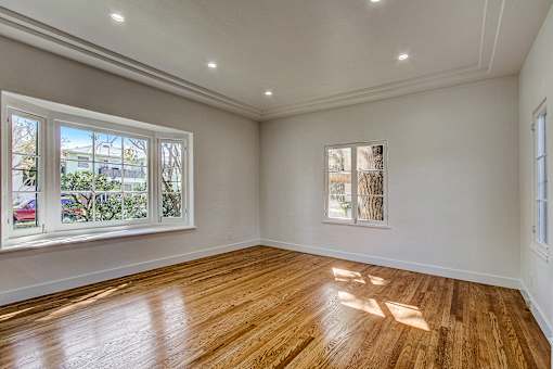 A room with wooden floors and white walls, with windows showing an outdoor view.