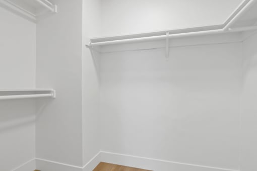 A white closet with two shelves and a wooden floor.