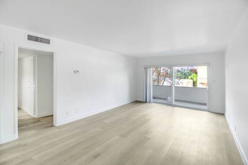 A room with a white wall and a window with a view of trees and a building outside.