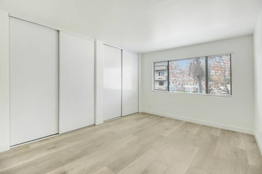 A room with white walls, a window with blinds, and a wooden floor.