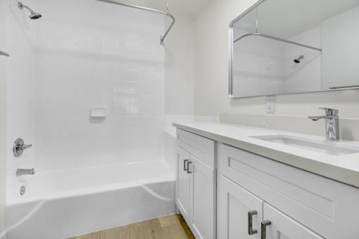 A white bathroom with a sink, mirror, and bathtub.