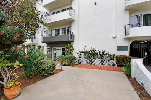 A white building with a balcony and a small garden in front.