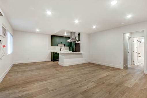 A spacious room with wooden flooring and a kitchenette in the corner.
