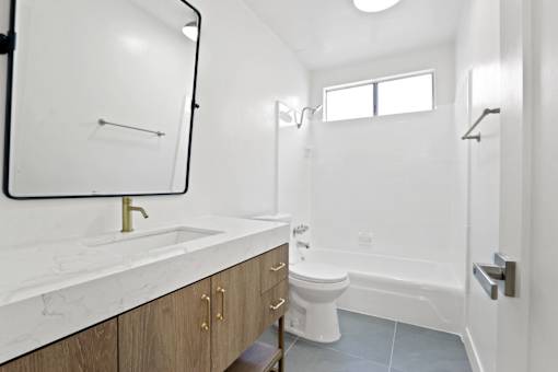 A white bathroom with a marble counter top and a toilet.