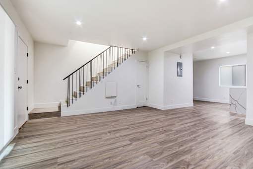 A spacious room with wooden flooring and a staircase with a metal railing.