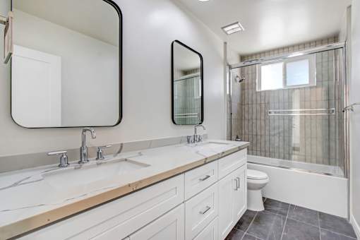 A white bathroom with a double sink and a toilet.