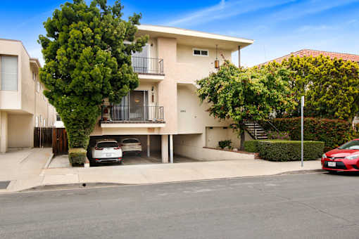 A white two-story apartment building with a red car parked in front.