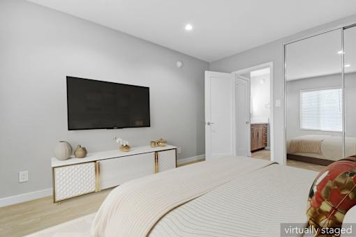 A bedroom with a large bed, a flat screen TV, and a mirrored doorway leading to another room.