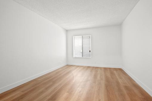 A room with wooden flooring and a window with blinds.