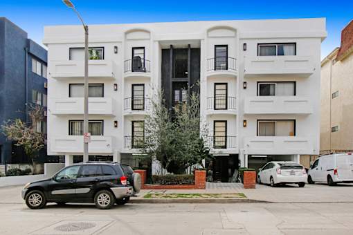 A black SUV is parked in front of a white building with a tree in front of the building.