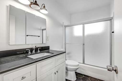 A white bathroom with a sink, mirror, toilet and shower.