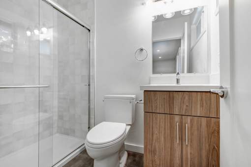 A white toilet sits in a bathroom with a wooden cabinet and a glass shower door.