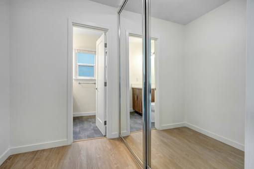 A room with a wooden floor and white walls, with a mirror on the wall.
