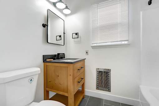 A white bathroom with a wooden vanity and a white toilet.