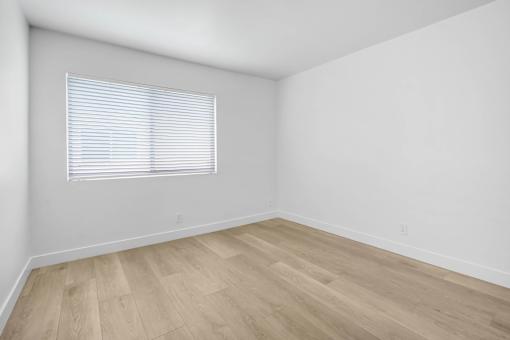 A room with wooden flooring and a window with blinds.