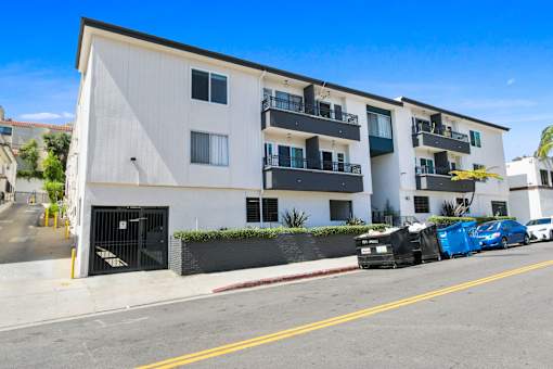 A blue car is parked on the street in front of a white building.