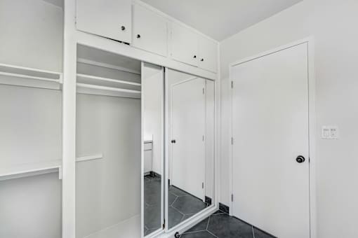 A white closet with a mirror and shelves.