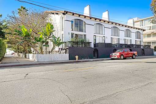 A red car is parked on the side of a street in front of a white building.