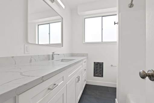 A white bathroom with a marble counter top and a large mirror.
