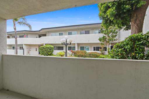 A white building with a balcony and a tree in front.