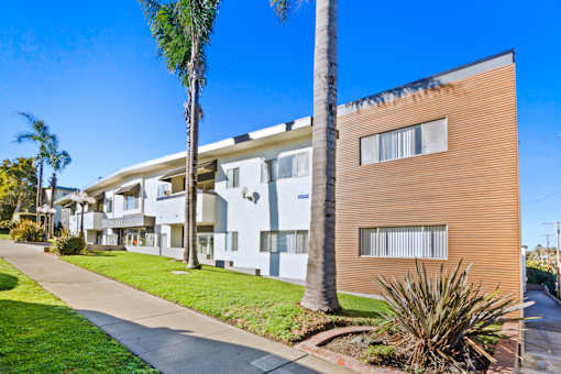 A row of modern apartment buildings with palm trees in front.