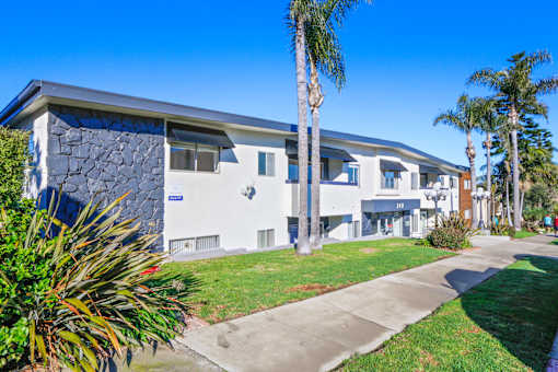 A modern building with a stone facade and palm trees in front.