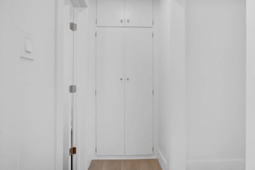 a long white hallway with two white closets and a wood floor