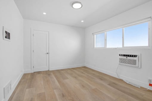 a living room with white walls and wood flooring and a door and window
