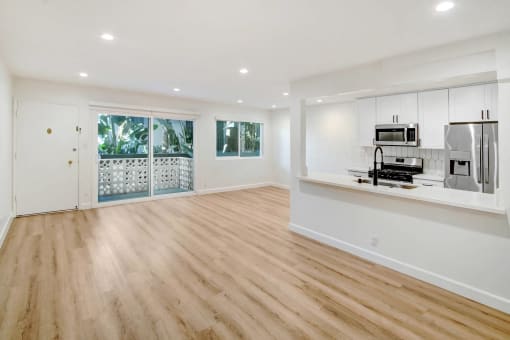 an empty living room with a kitchen and a door to a balcony