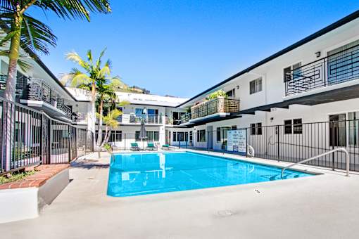 A swimming pool in a sunny courtyard surrounded by buildings.