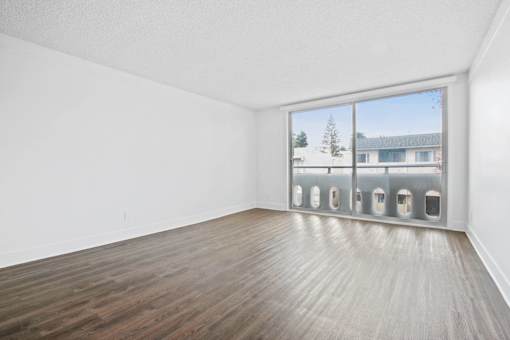 Empty room with wooden floor and a window showing a tree and a building outside.
