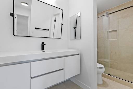 A white bathroom with a sink, mirror, toilet and shower.