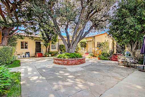 A courtyard with a tree in the center and a house in the background.
