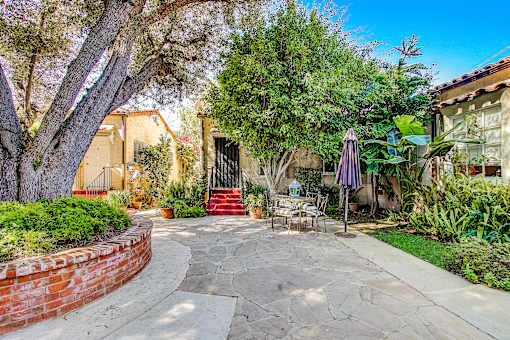 A patio with a table and chairs is surrounded by greenery.