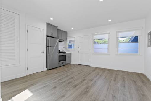 A spacious kitchen with wooden flooring and white walls.