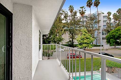 A balcony with a white wall and a red car in the background.