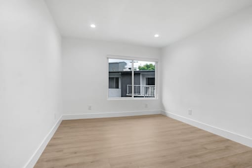 A room with wooden flooring and a window showing a building outside.