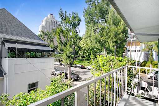 A balcony with a white railing overlooks a parking lot and trees.