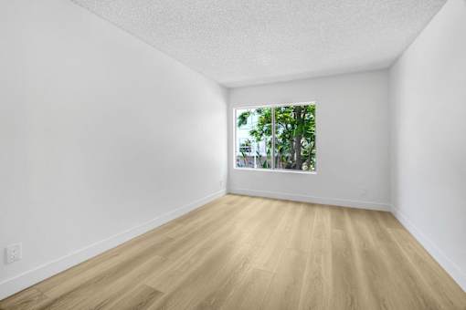 A room with wooden floors and a window showing trees outside.