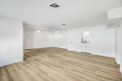 A spacious room with wooden flooring and white walls.