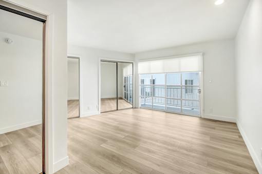 A spacious room with wooden flooring and a view of a cityscape through the windows.