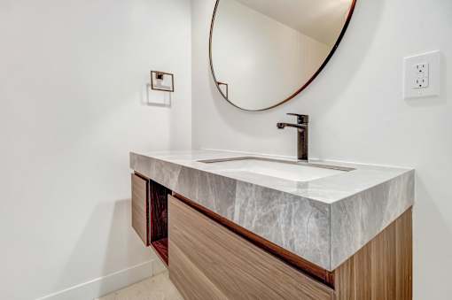 A bathroom sink with a marble countertop and a round mirror above it.