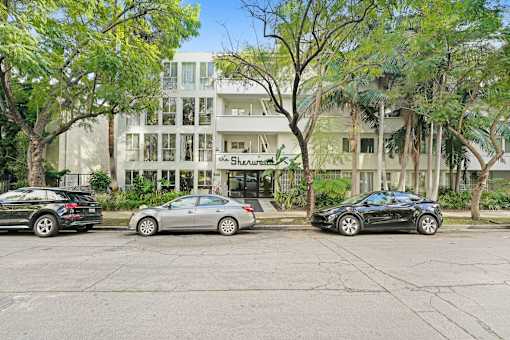 Three cars are parked in front of a white building with the name Shearman on it.