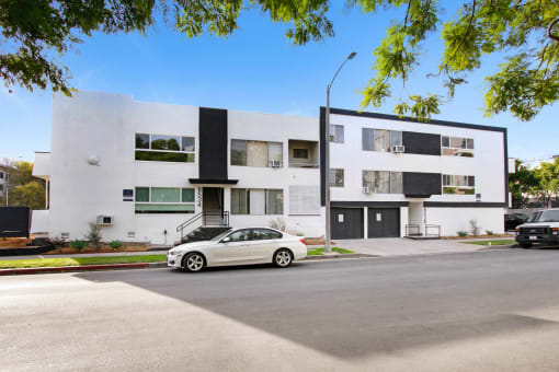 a white car parked in front of a white and black apartment building