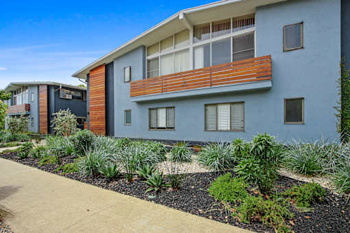 A modern two-story building with a balcony and a garden in front.