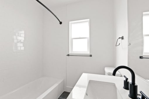 a white bathroom with a tub and a sink and a window