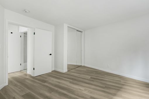 A room with white walls and wooden flooring with two doors.